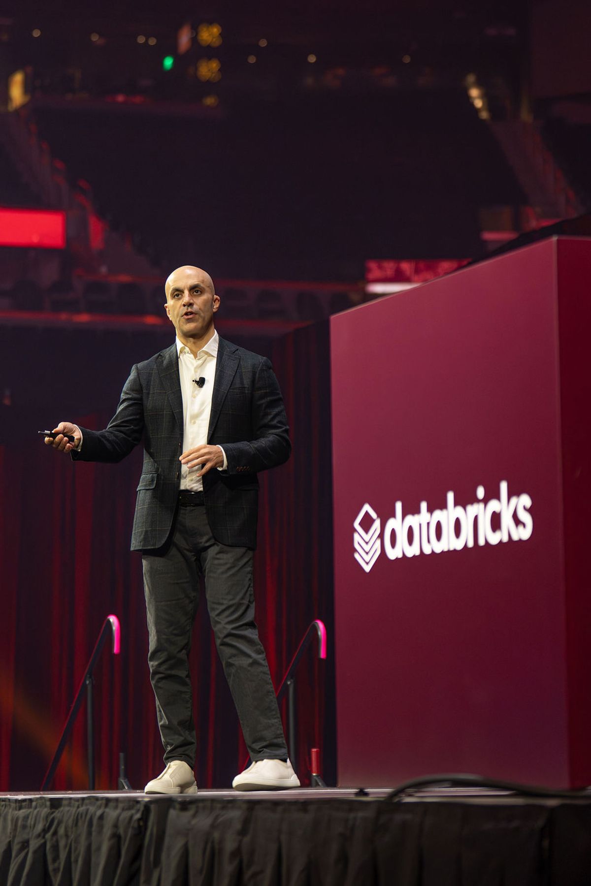 Bald speaker in dark suit presenting on stage with microphone and Databricks branded podium at conference