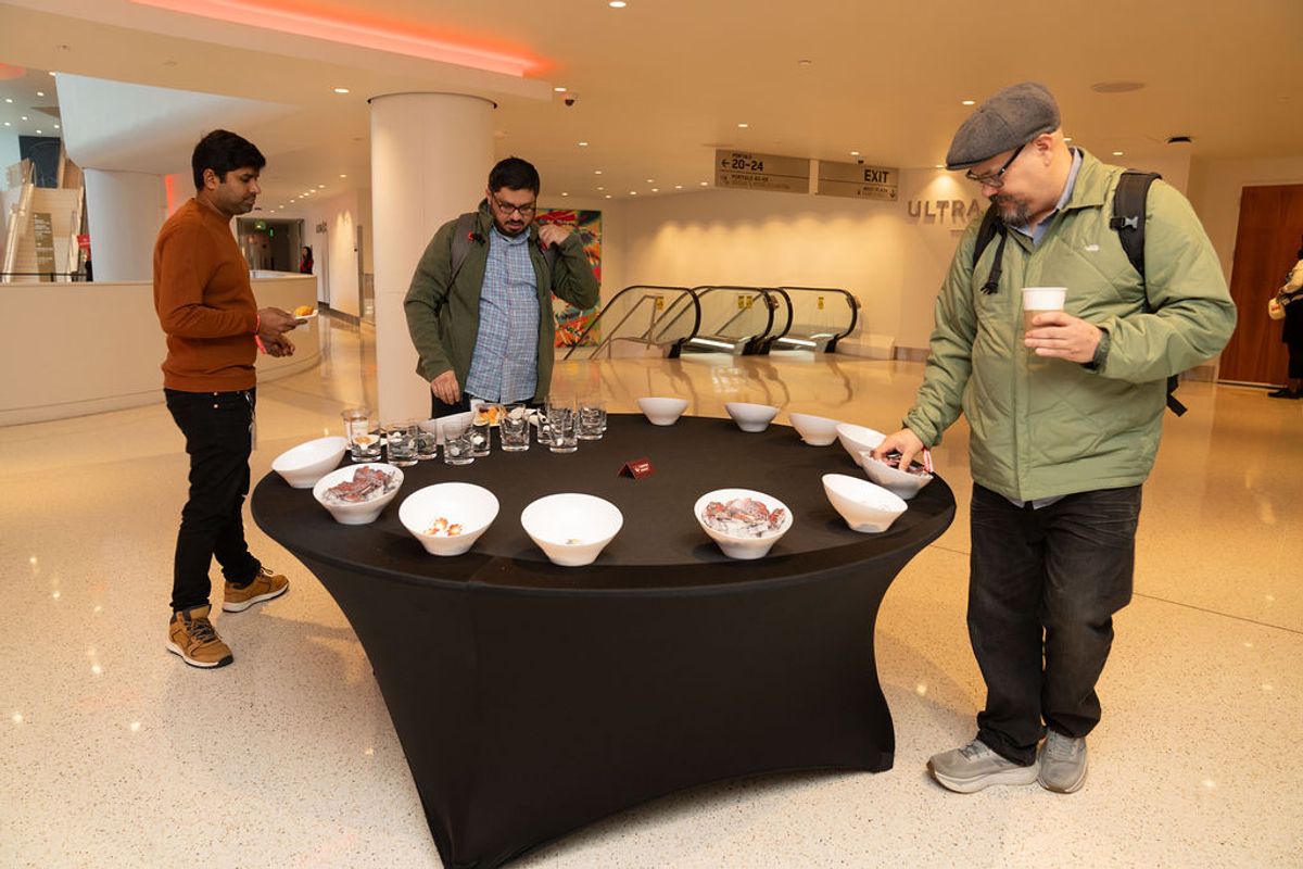 Three men at refreshment table with bowls of snacks and beverages in modern building lobby