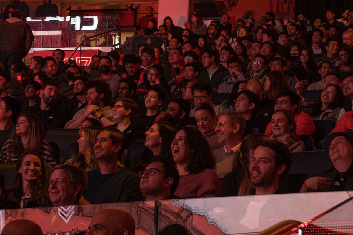 Large crowd of attendees laughing and smiling while seated in tiered seating at an indoor event venue