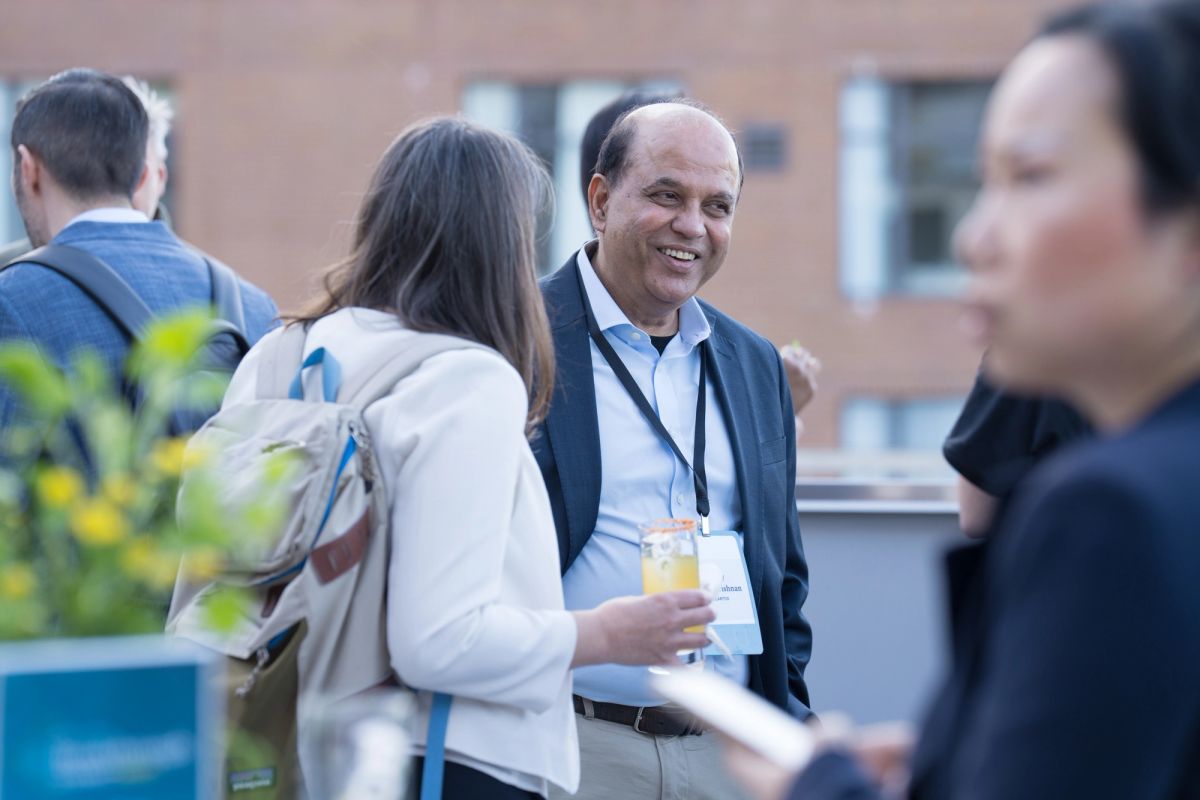 Conference attendees networking outdoors, with a smiling man in business casual attire speaking with.