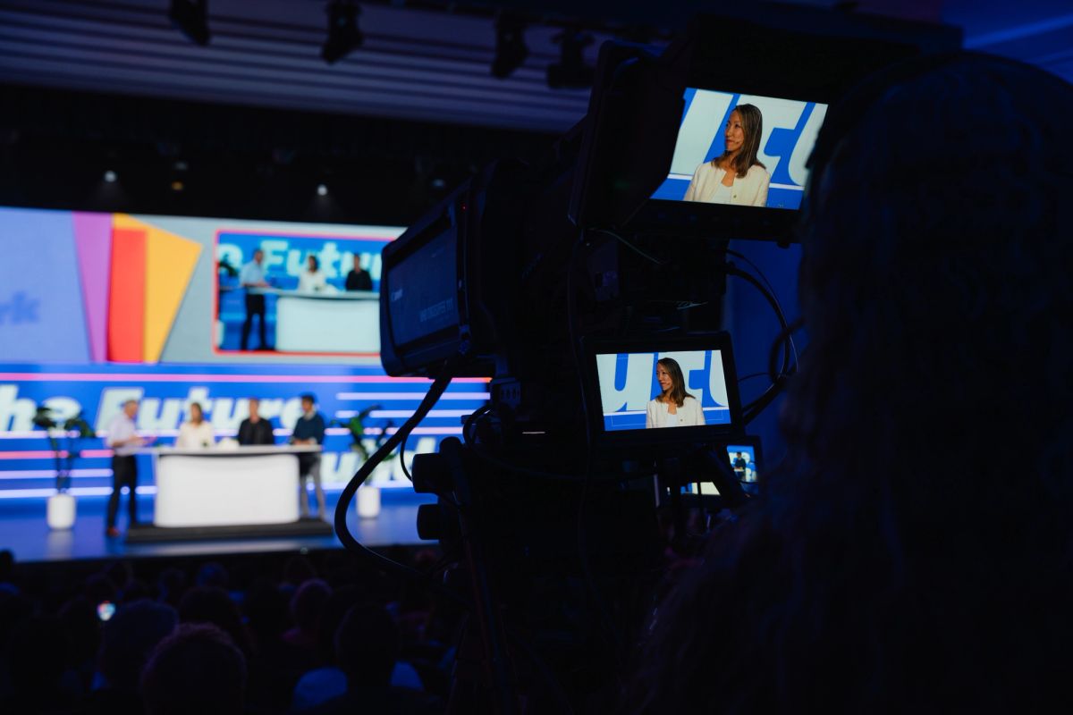 Television camera filming a news studio with anchor at desk and colorful backdrop