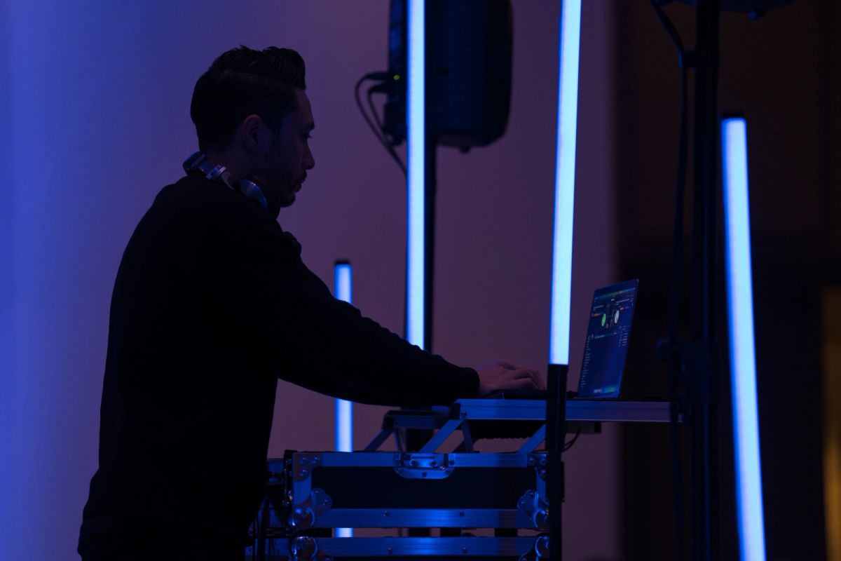 DJ performing at event setup with laptop and equipment under blue stage lighting