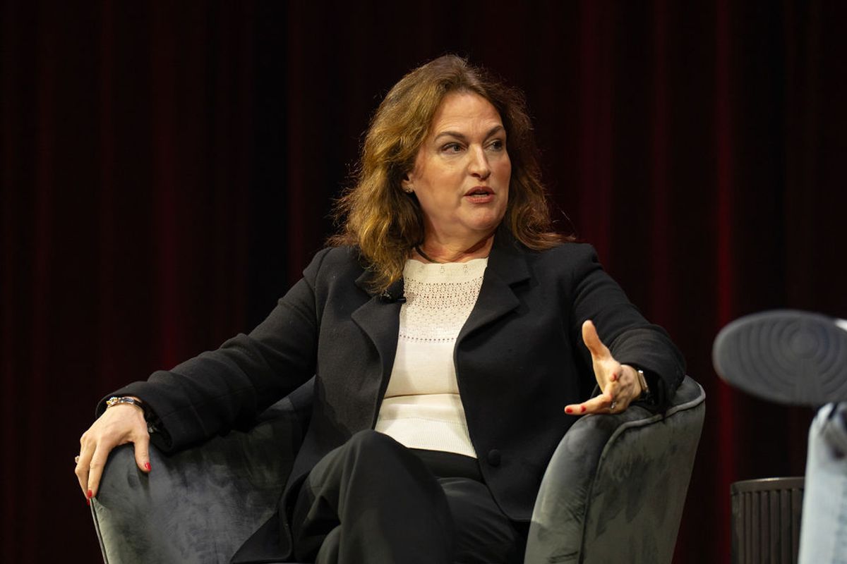 Executive speaking at conference panel, seated in dark armchair making gestures while addressing audience