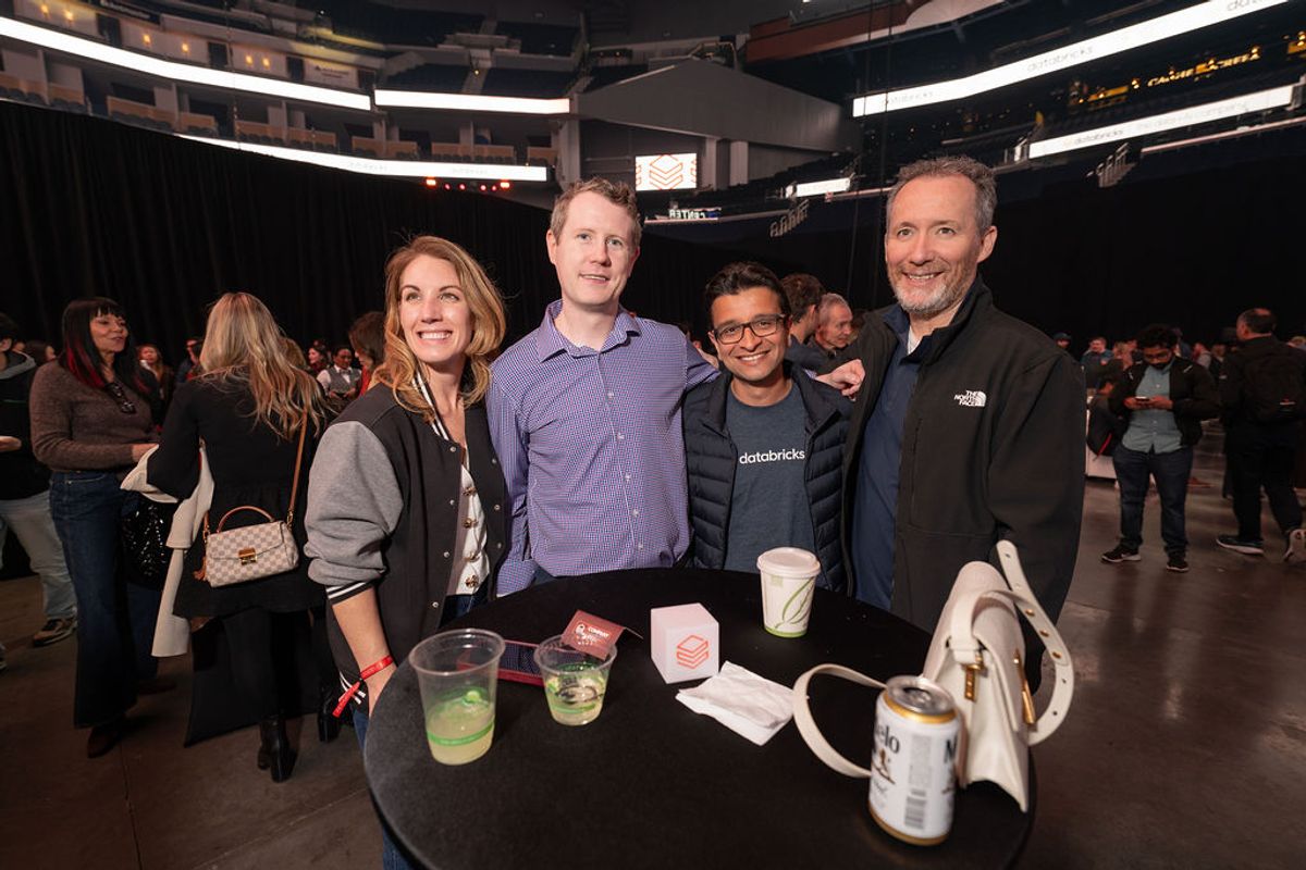 Four people networking at a conference event, standing around a cocktail table with drinks in a large venue