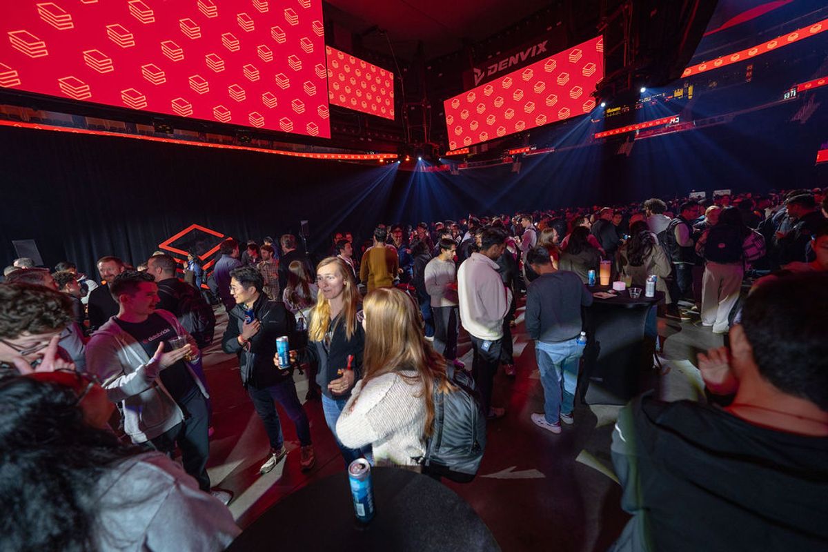 Large crowd of conference attendees networking in arena venue with red branded screens overhead