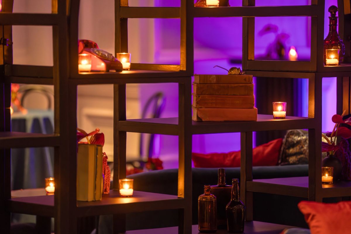 Elegant shelving display with candles, bottles, and decorative objects lit with warm purple and orange.
