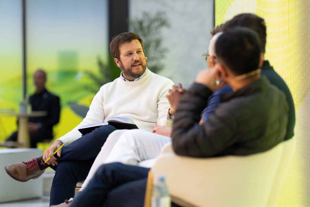 Three attendees in conversation at a conference, seated casually in a bright modern venue.