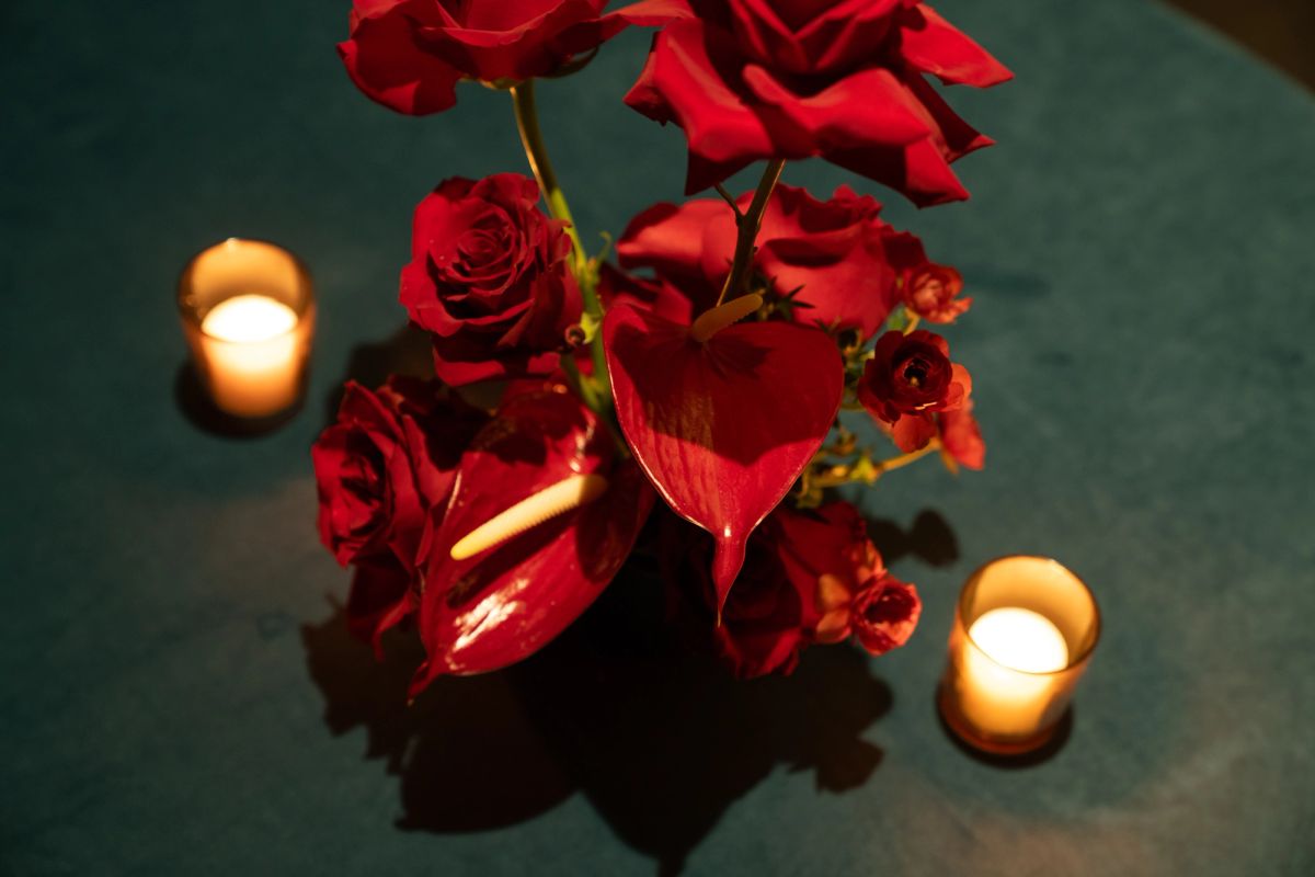 Red roses and heart-shaped petals arranged with glowing candles on dark surface creating romantic ambiance
