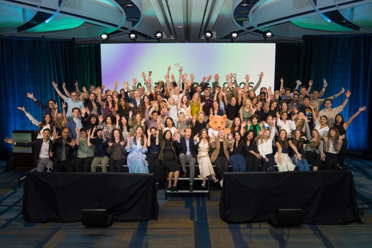 Large group of conference attendees posing with hands raised on a ballroom stage.