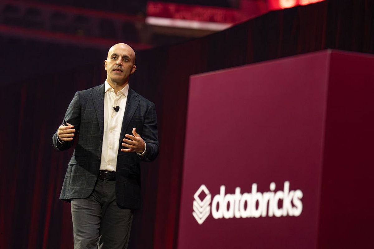 Speaker presenting on stage with red Databricks backdrop at conference venue