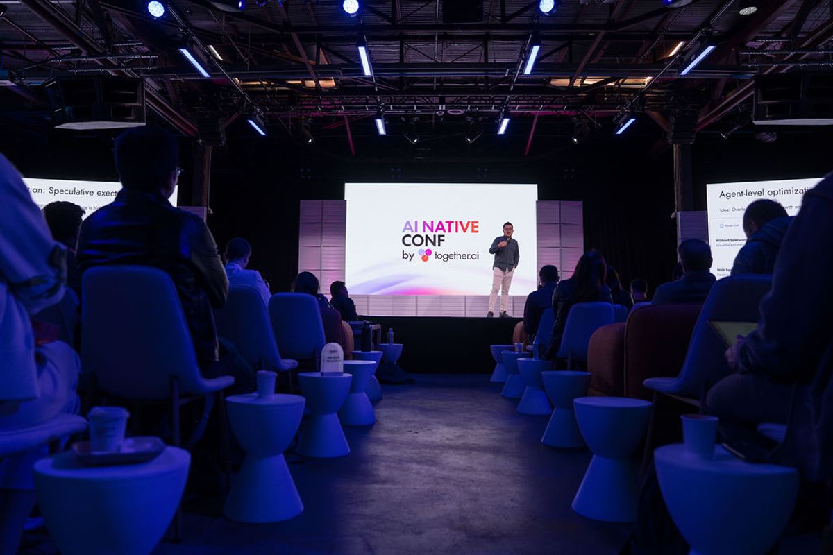 Speaker presenting at AI Native Conference to seated audience in dimly lit venue with blue lighting
