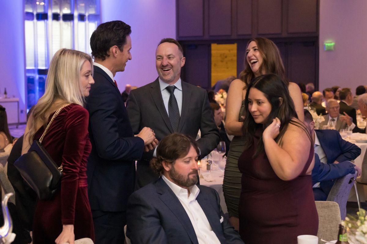 Group of formally dressed attendees socializing and laughing at an upscale evening gala event