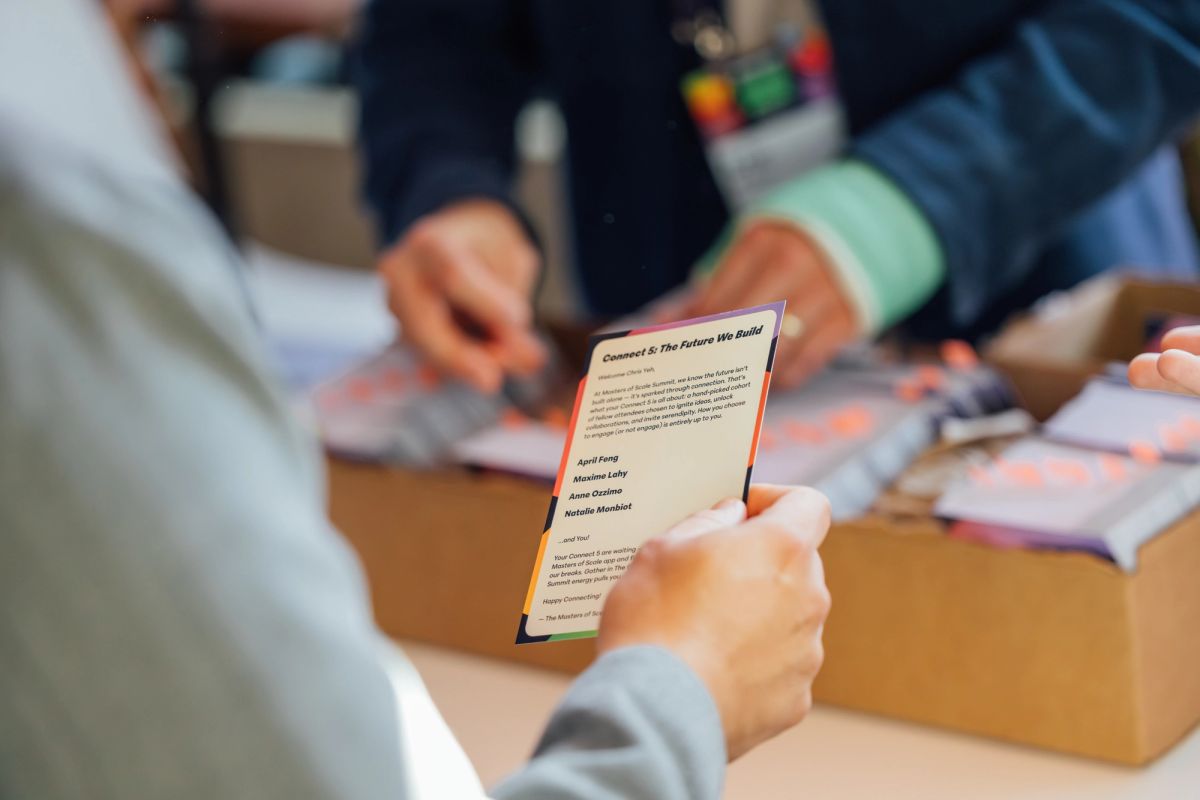 Attendee holds conference program card while others review materials at table during event