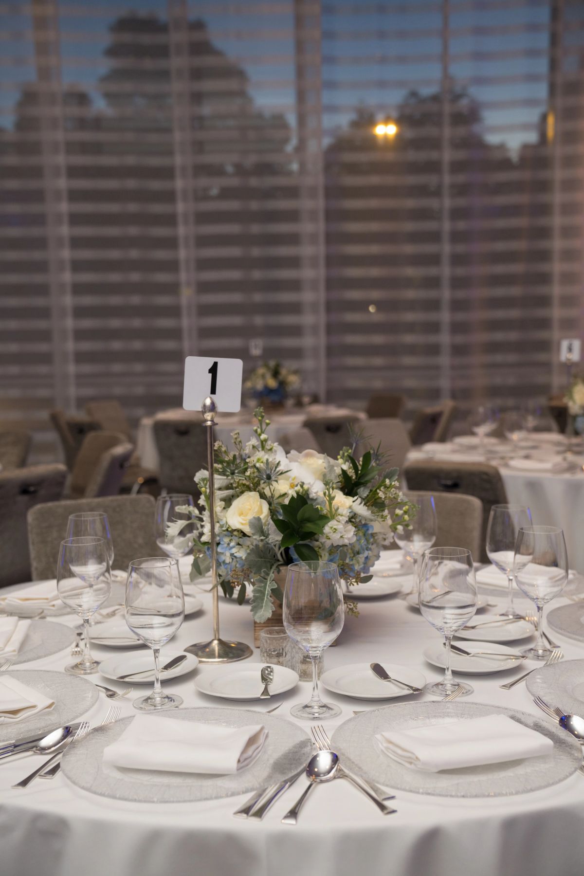 Elegant round table with white linens, floral centerpiece, wine glasses, and formal place settings.