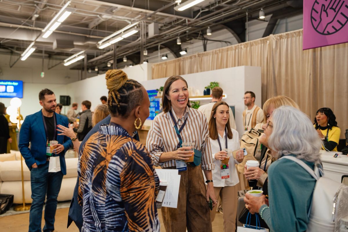 Attendees networking and conversing at an indoor conference event in a modern venue with exposed ceiling.