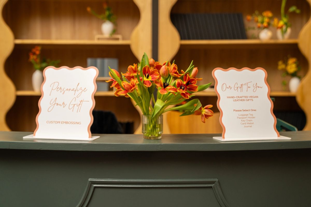 Two decorative signs flanking orange flowers in a vase on a counter, with hexagonal shelving displaying items.