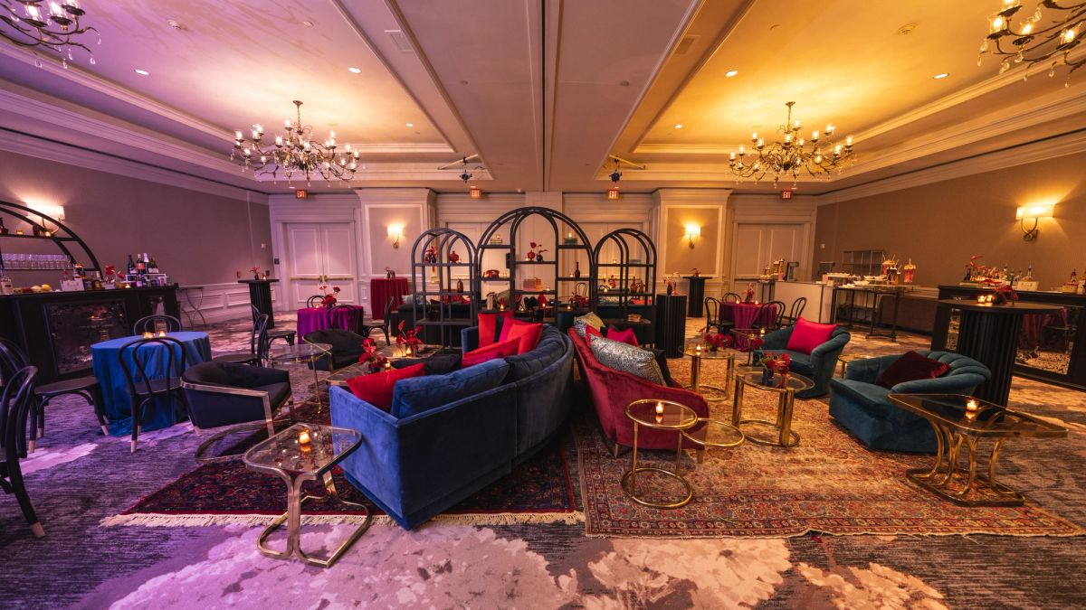 Elegant hotel lounge with velvet sofas, ornate chandeliers, and colorful ambient lighting in purple and gold.