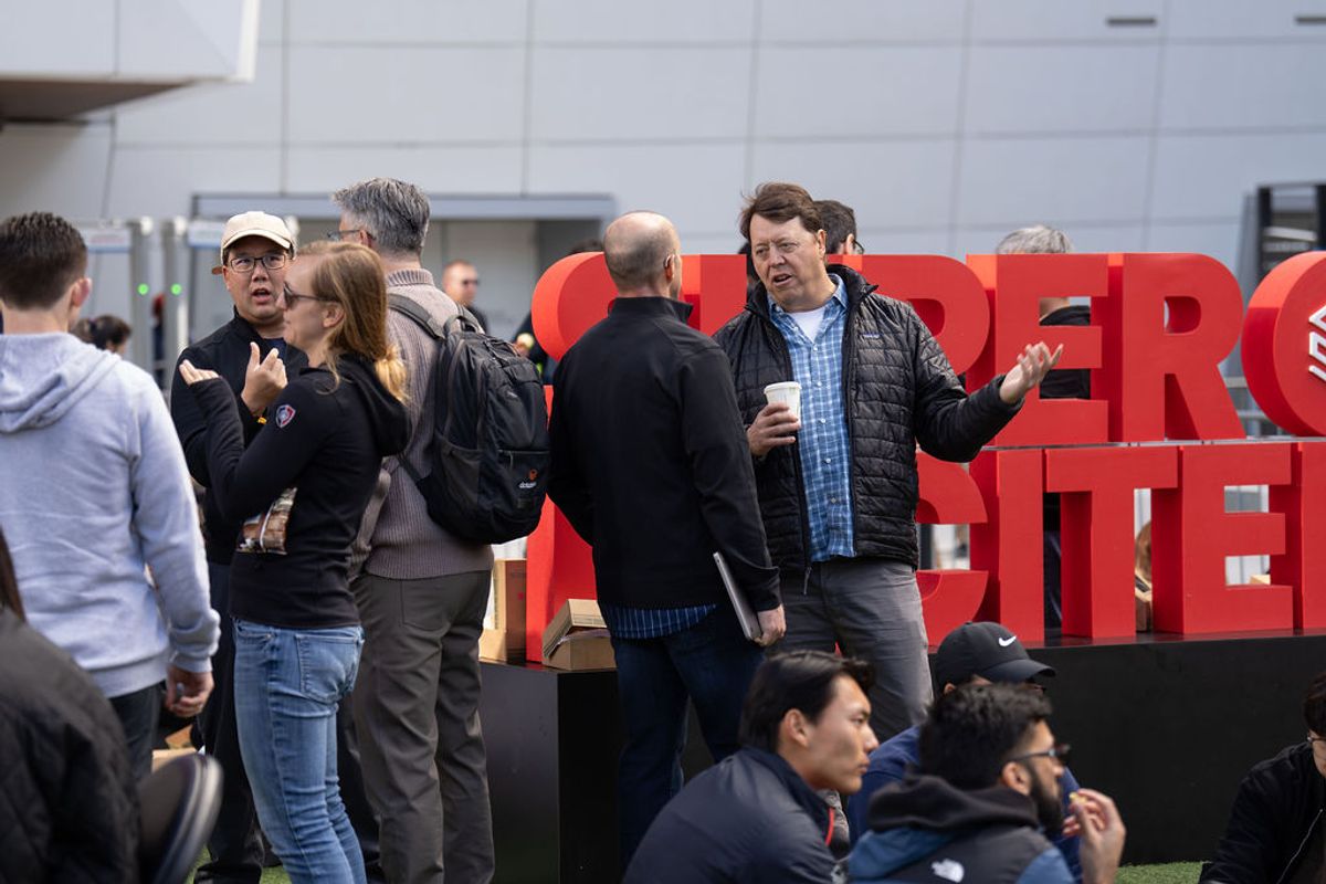 Conference attendees networking and conversing in front of large red letter signage at an indoor venue