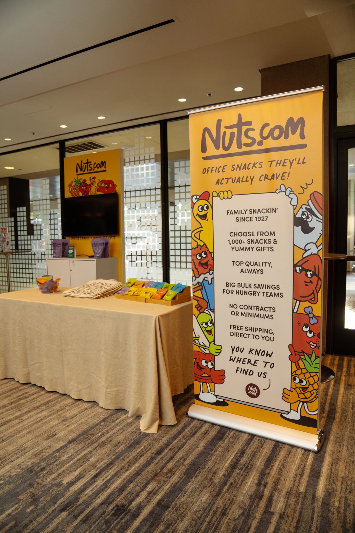 Nuts.com branded display banner and snack table at a conference expo area.