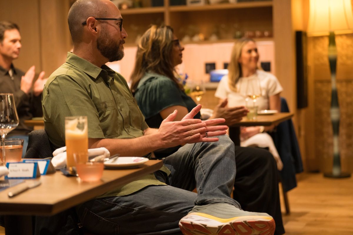 Bald man with glasses in green shirt gesturing while speaking during panel discussion in kitchen setting