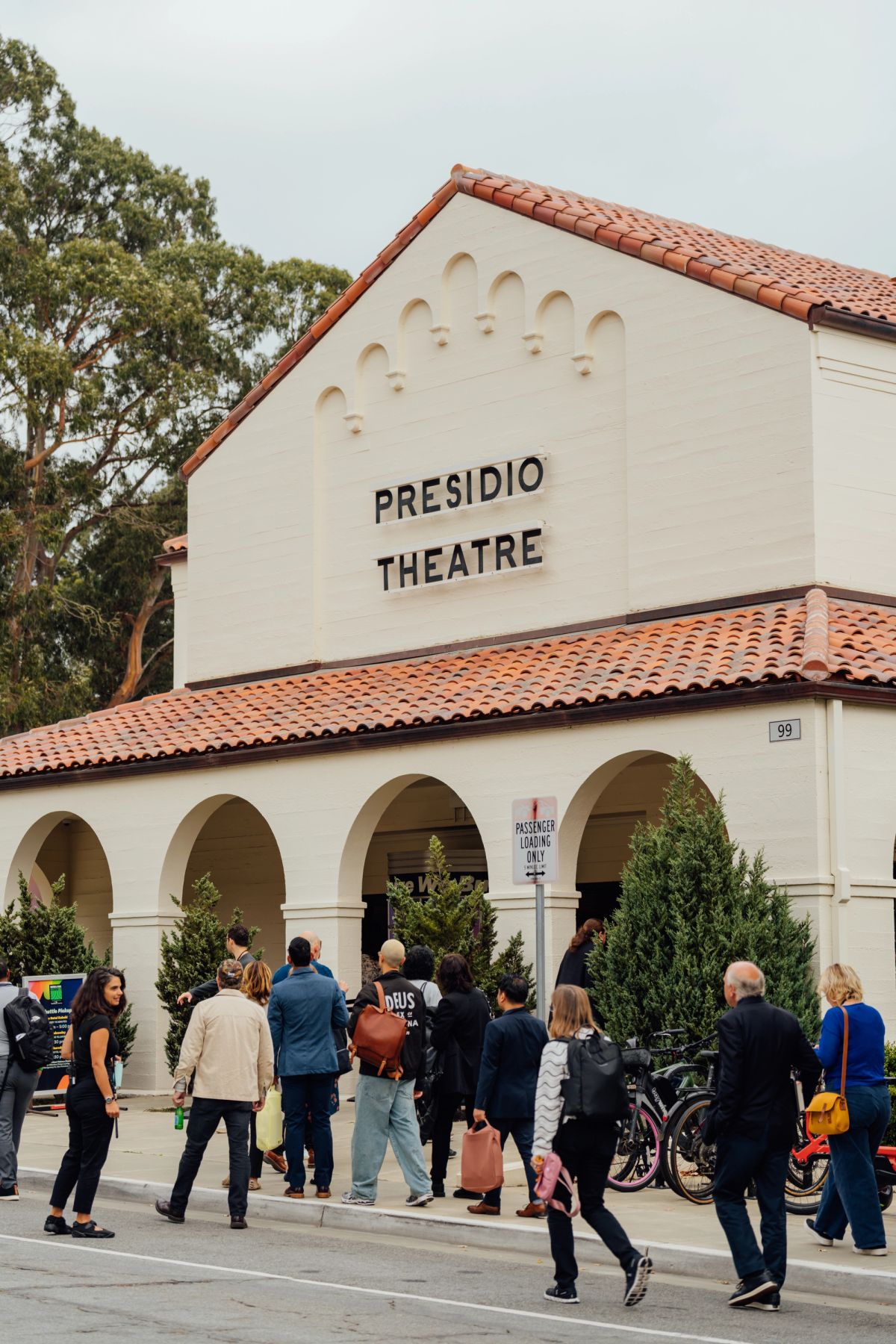 Attendees gather outside Presidio Theatre, a white building with red tile roof and arched entrance