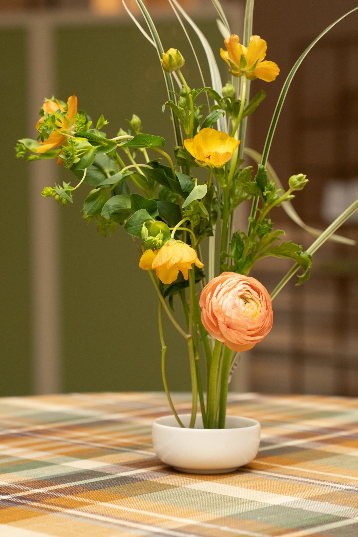 Fresh flower arrangement with yellow and pink blooms in white bowl on checkered tablecloth