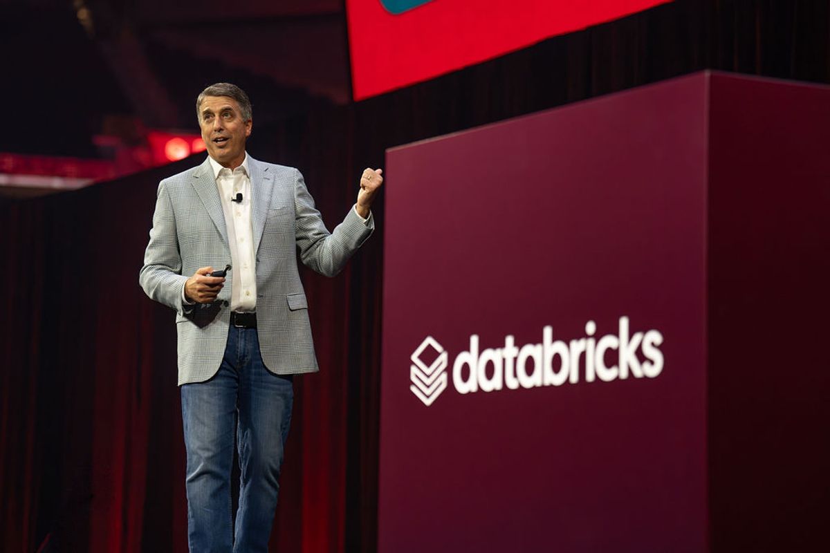 Speaker presenting on stage at Databricks conference, gesturing with raised fist while speaking at podium.