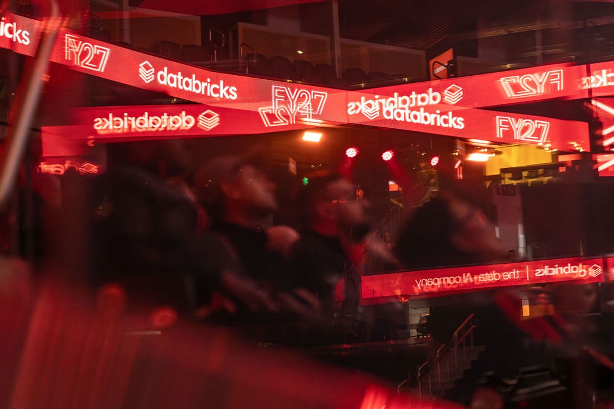 Red-lit event space with Databricks and FY27 branded banners overhead, attendees gathered below in conference.