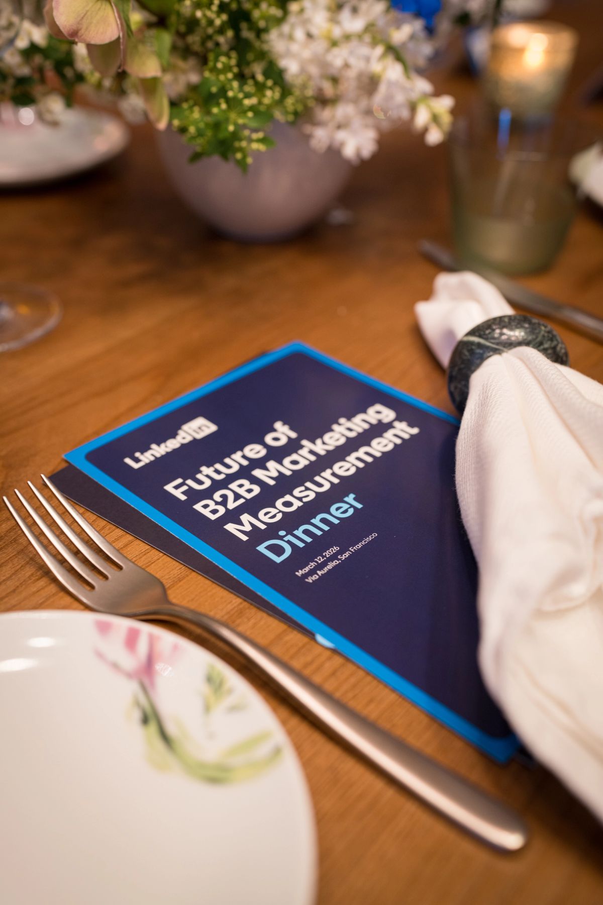 Elegant table setting with LinkedIn report titled "Future of B2B Marketing Measurement Dinner" beside napkin.