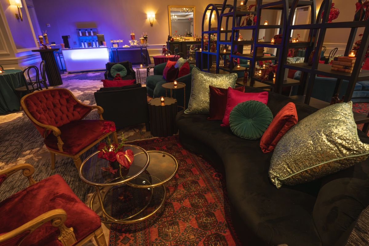 Elegant lounge area with dark sofas, red velvet chairs, gold coffee table, and colorful pillows in dimly lit.