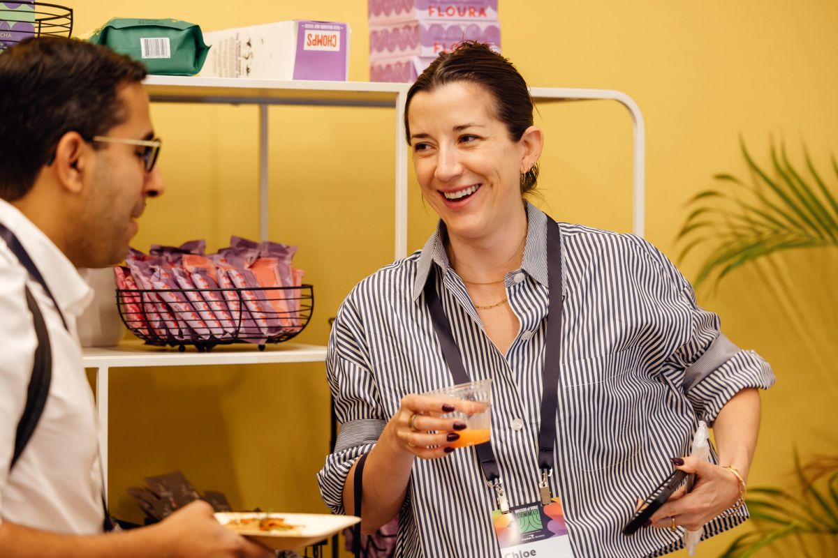 Two conference attendees networking and laughing while holding drinks and food at an indoor event