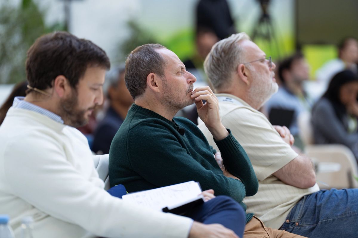 Three male attendees seated, listening attentively at an outdoor conference.