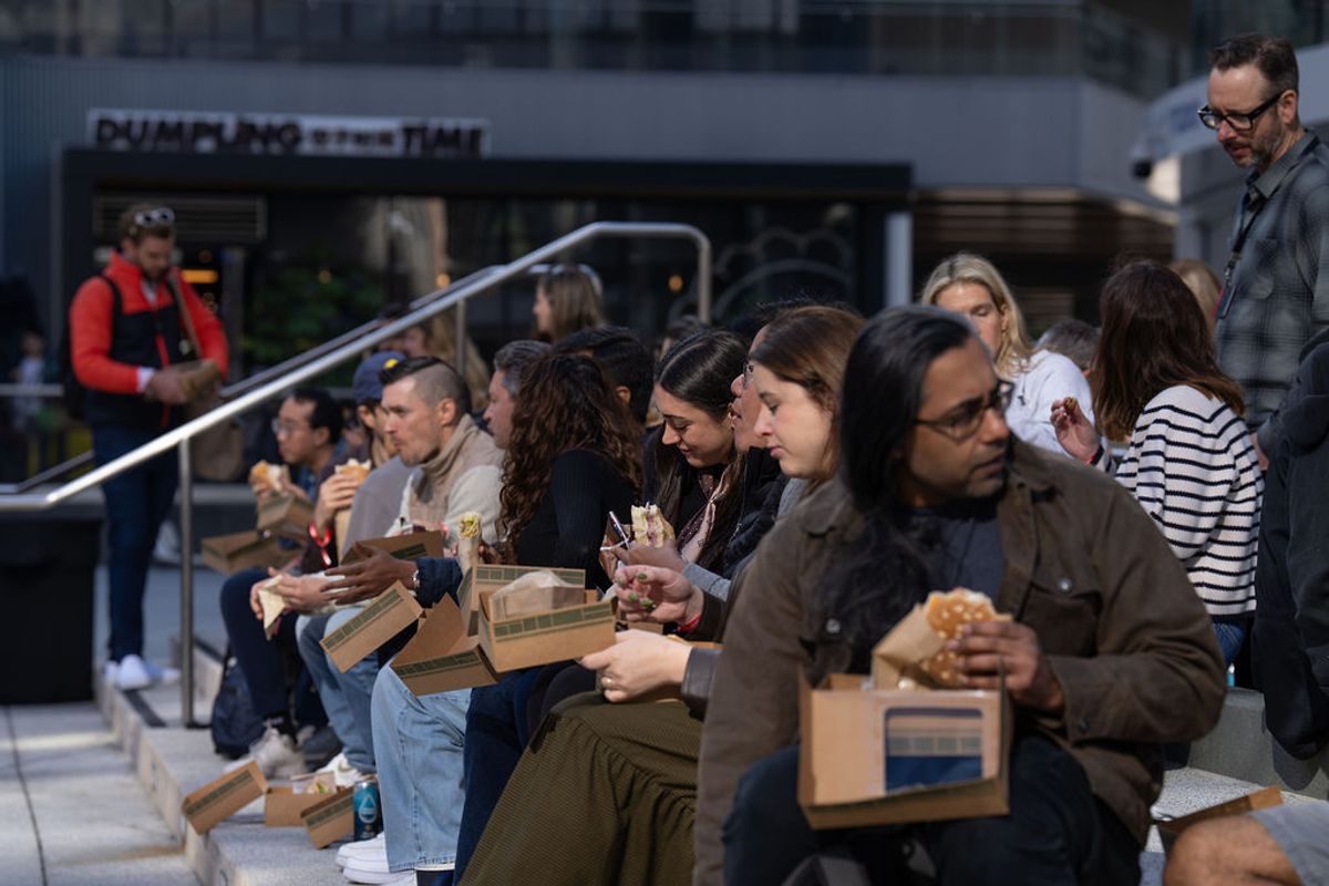 Conference attendees sitting on steps eating meals from boxes, with staff member standing nearby