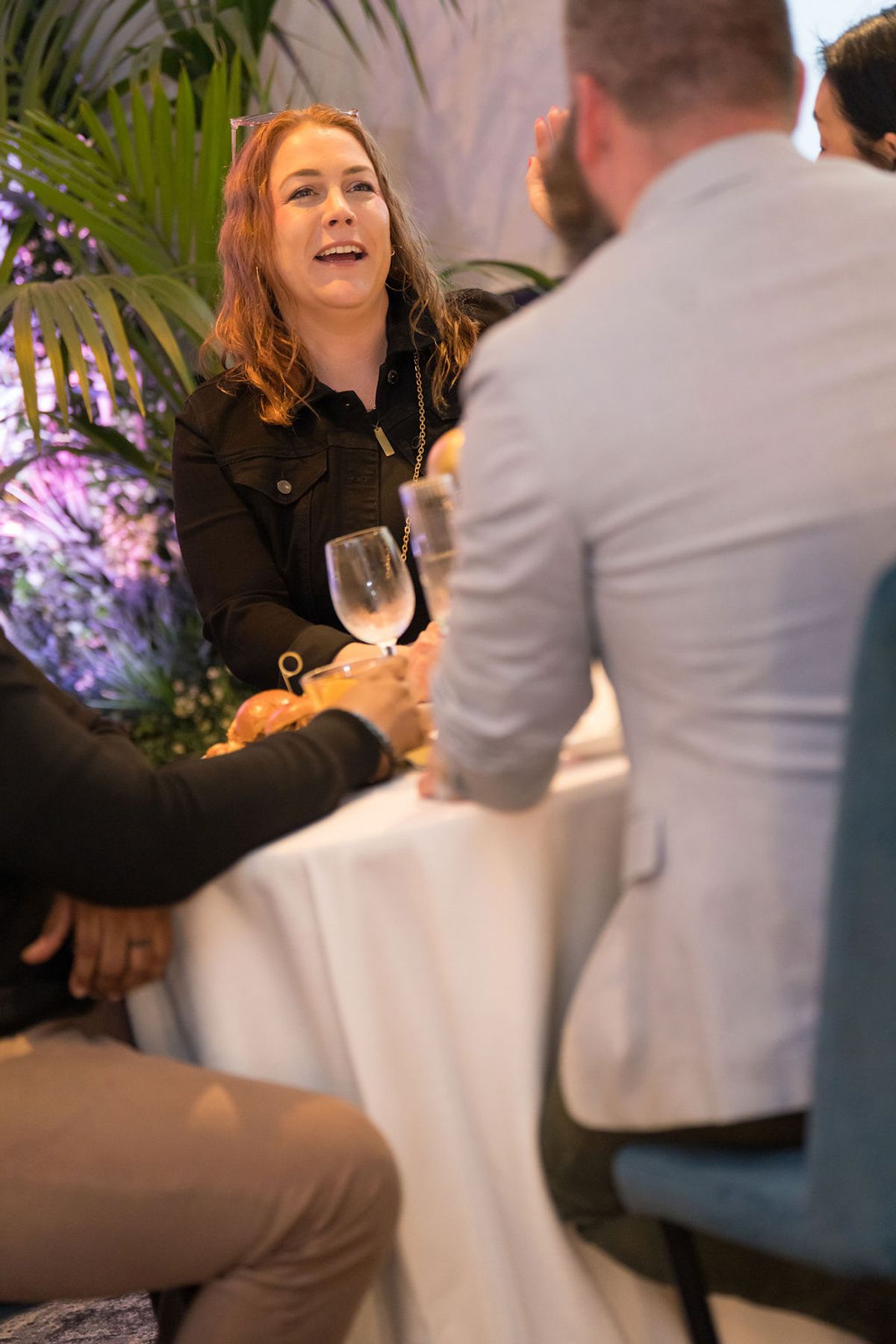 Woman in black jacket holds wine glass while talking with man in white shirt at networking reception