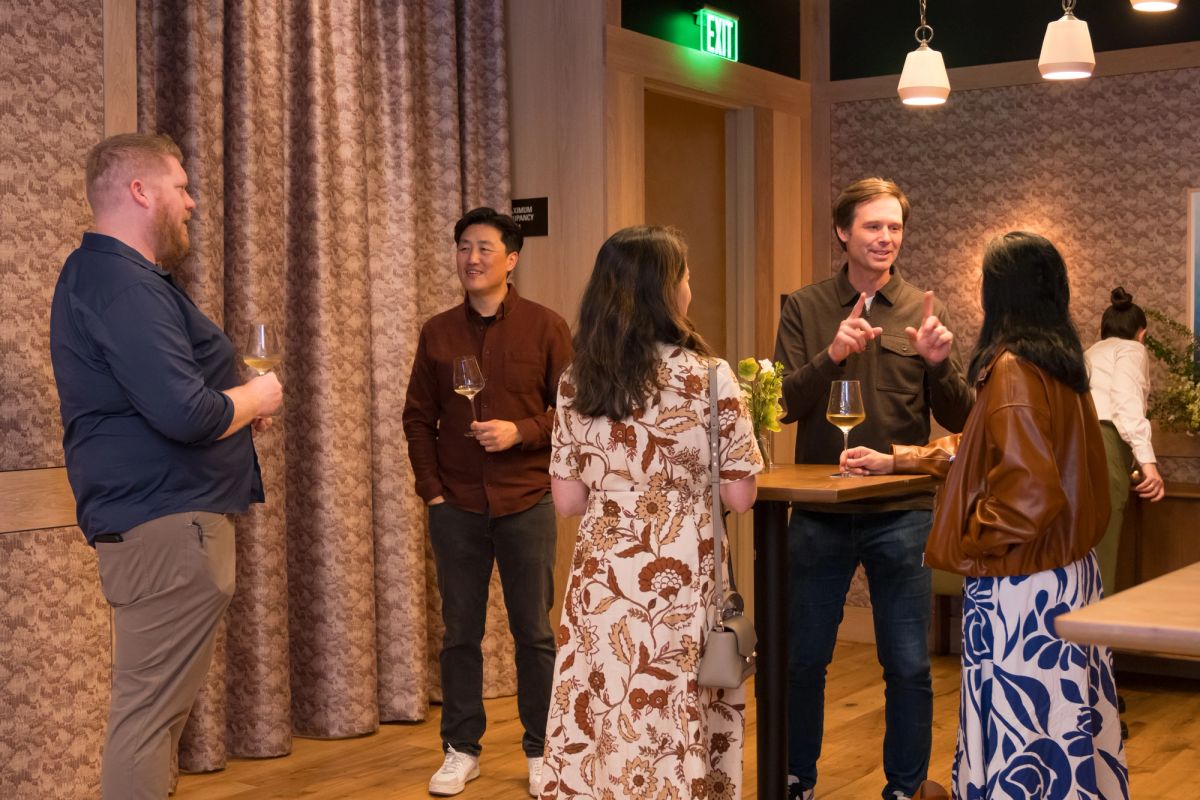 Five people networking with wine glasses in a modern restaurant setting with patterned wallpaper and pendant.