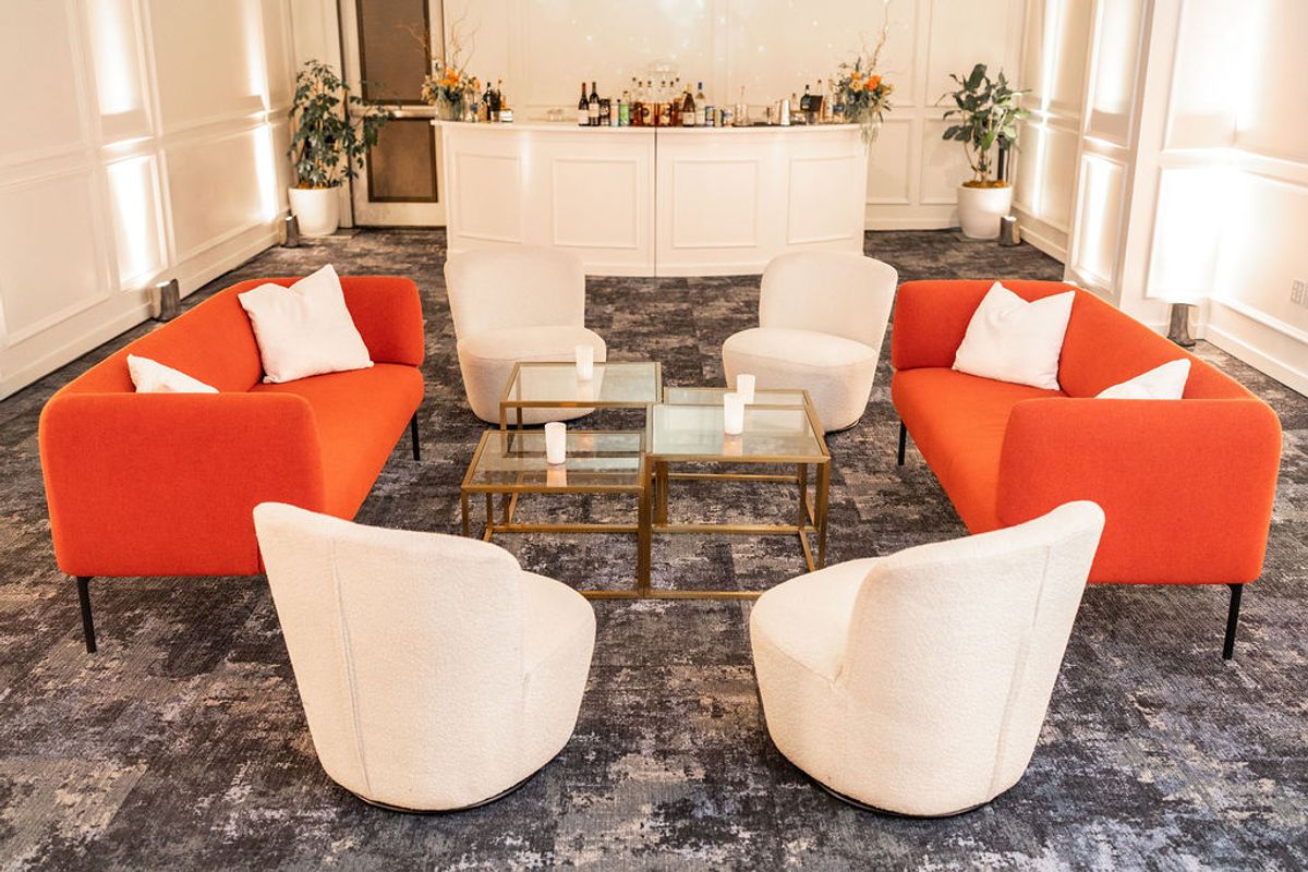 Orange sofas and cream chairs arranged around glass coffee table in elegant reception room with bar