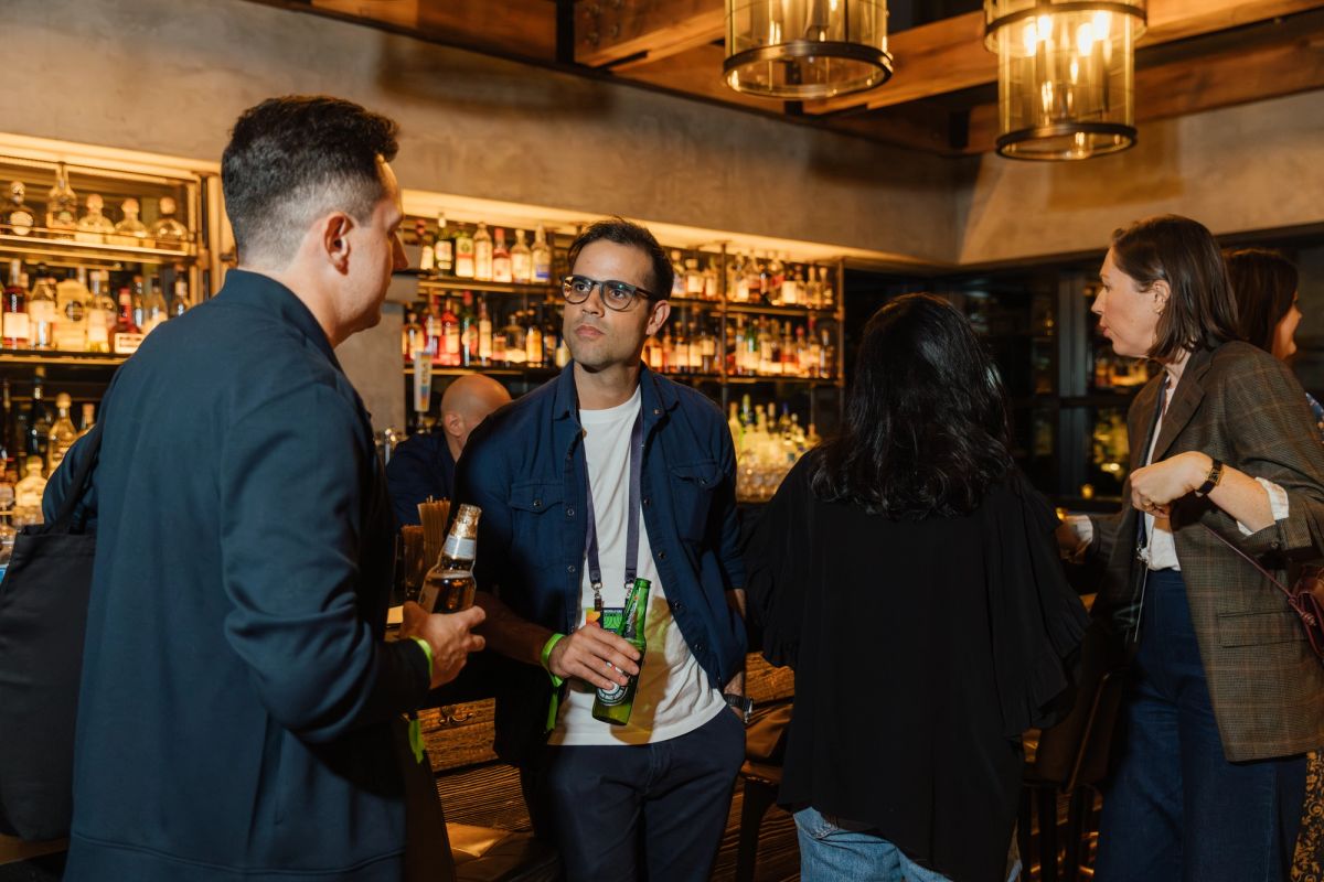 Attendees networking at a bar with exposed beams and bottles displayed on shelves behind them.
