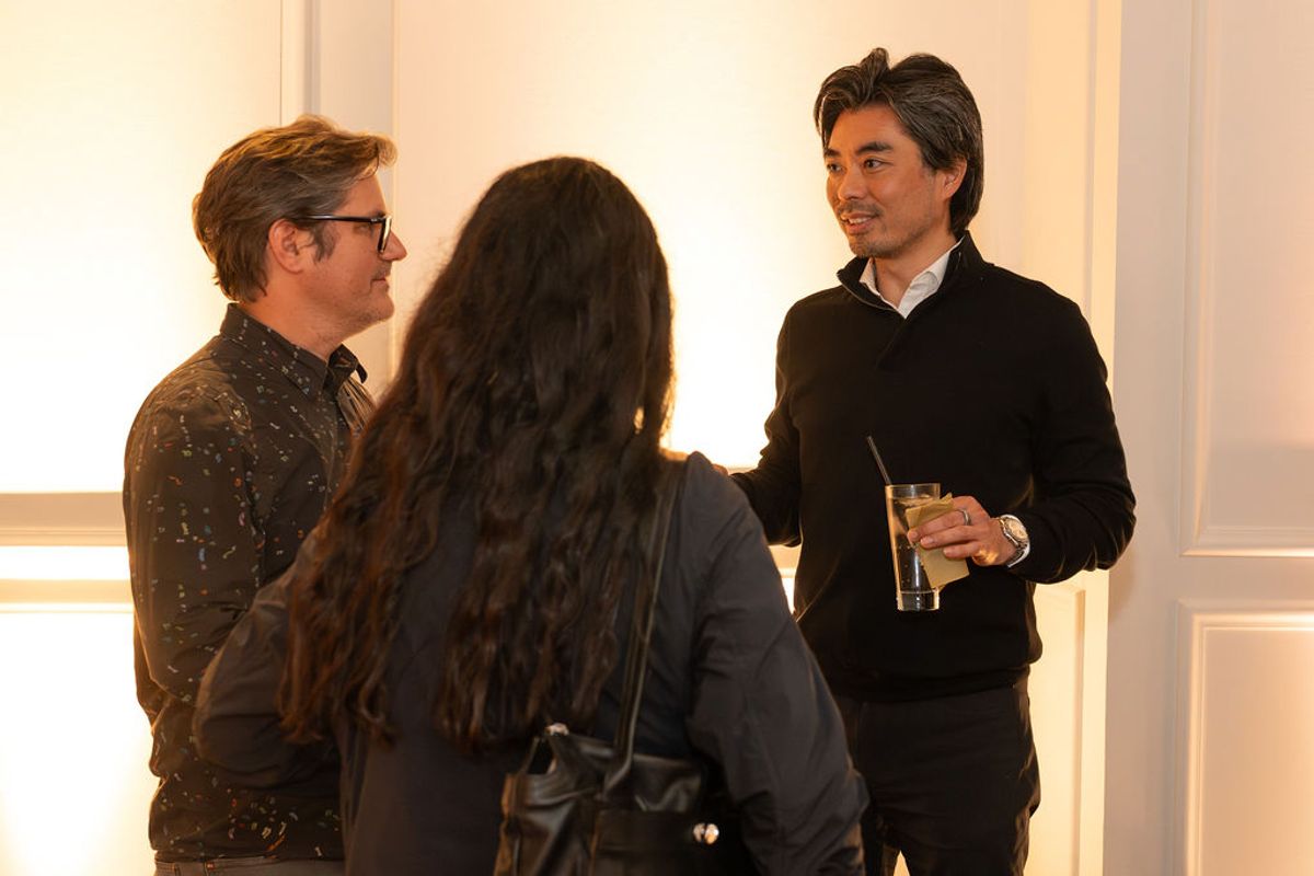 Three people networking at an indoor reception, with one man holding a drink while conversing.