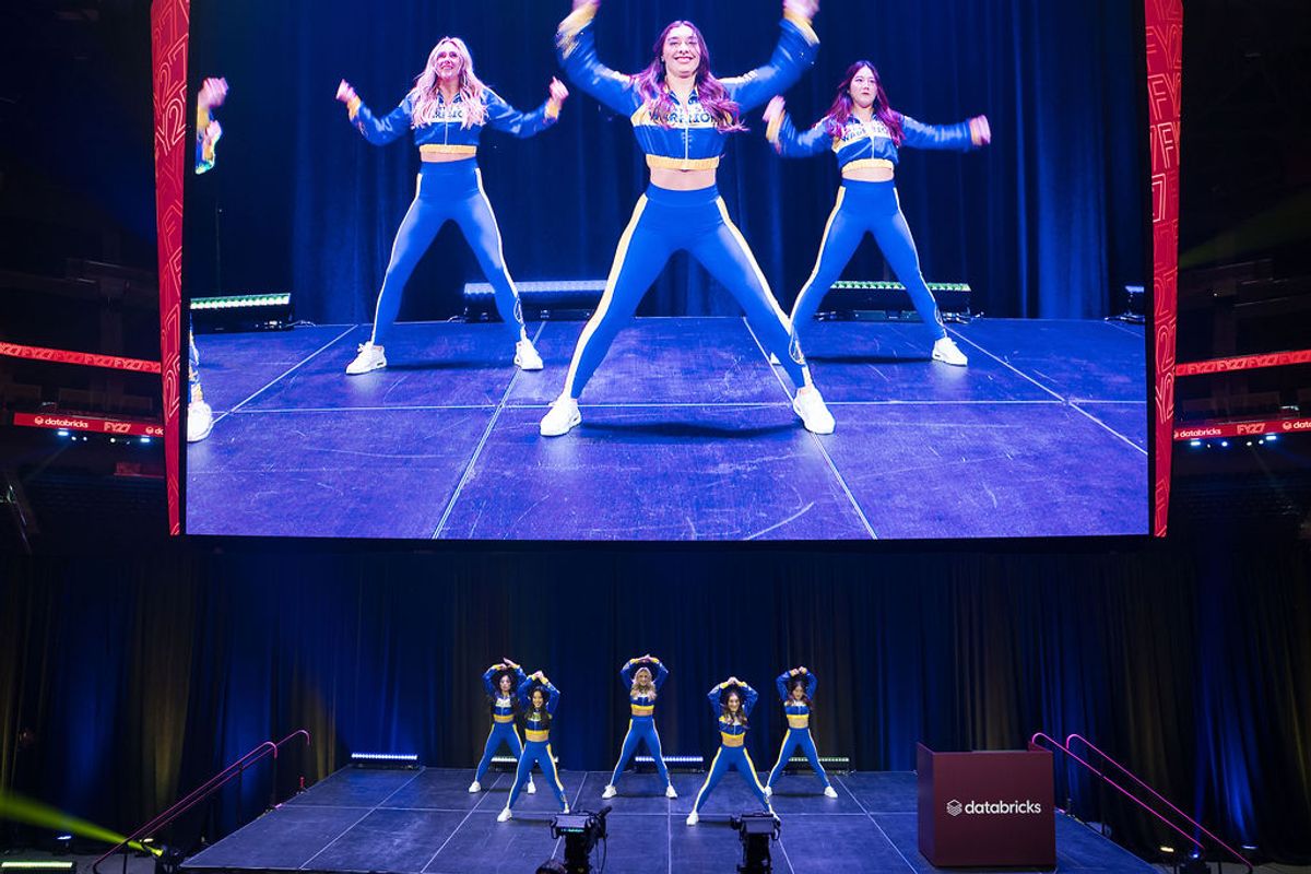 Performers in blue and white uniforms dancing on stage at conference venue with large screens above