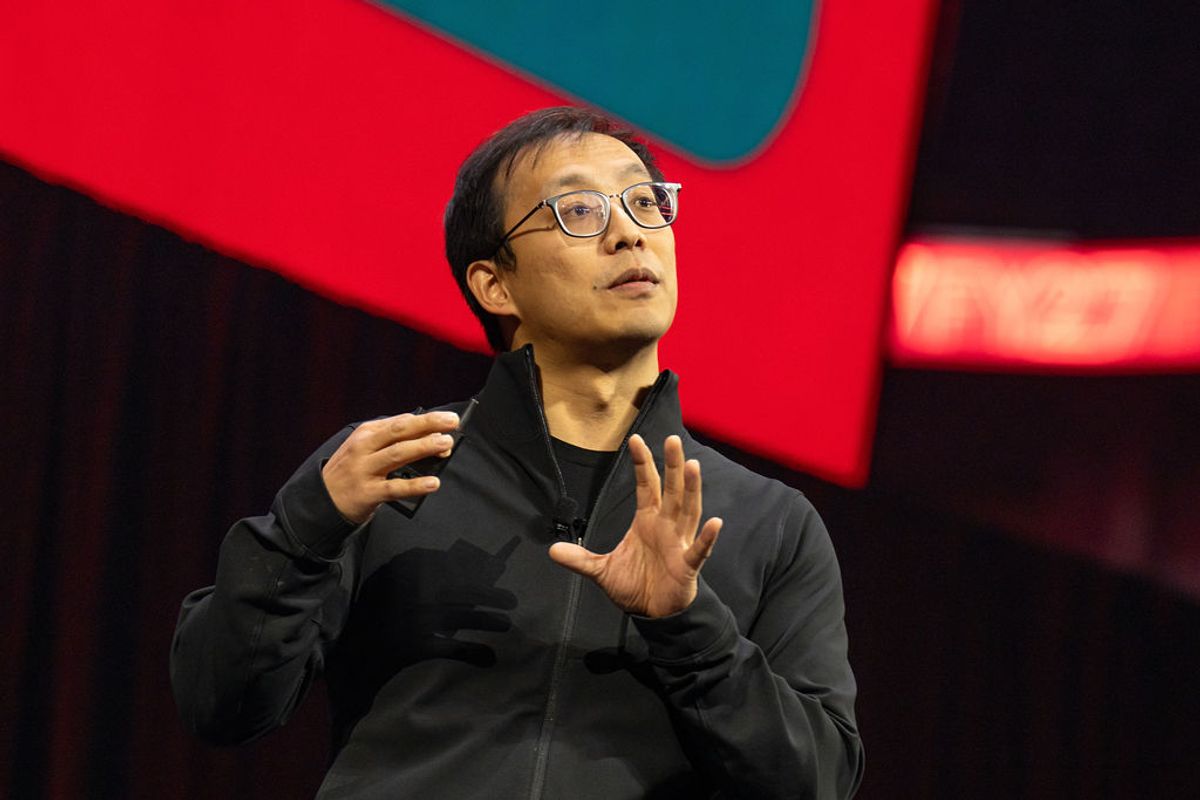 Speaker in glasses and dark sweater gesturing with hands during presentation on stage with colorful backdrop