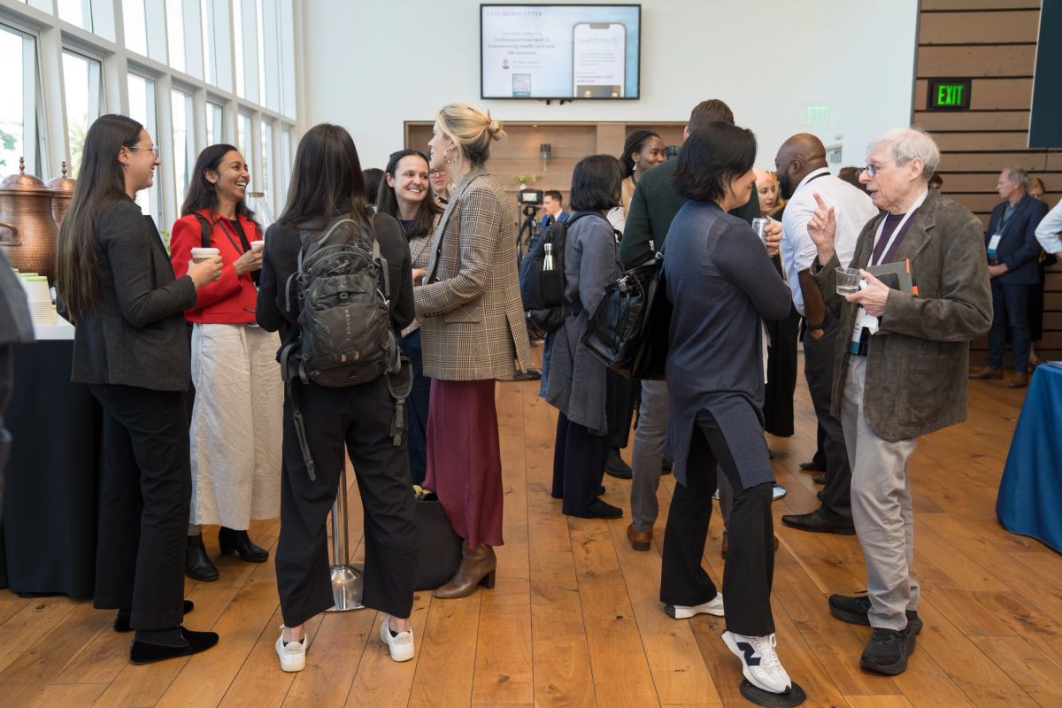 Attendees networking and conversing in groups at a conference event in a modern venue with large windows.