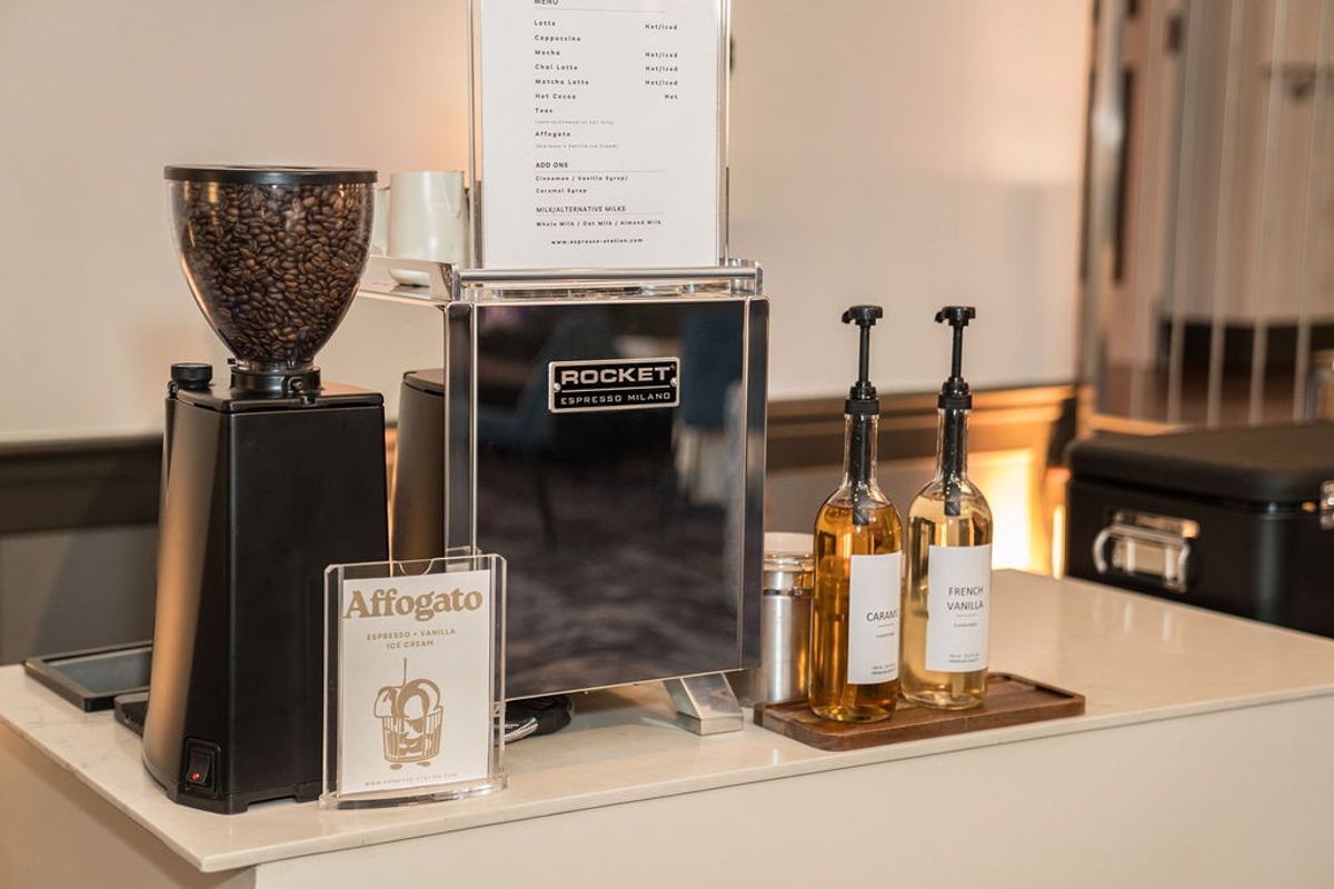 Coffee station with espresso machine, grinder, menu board, and bottles of syrup on white counter