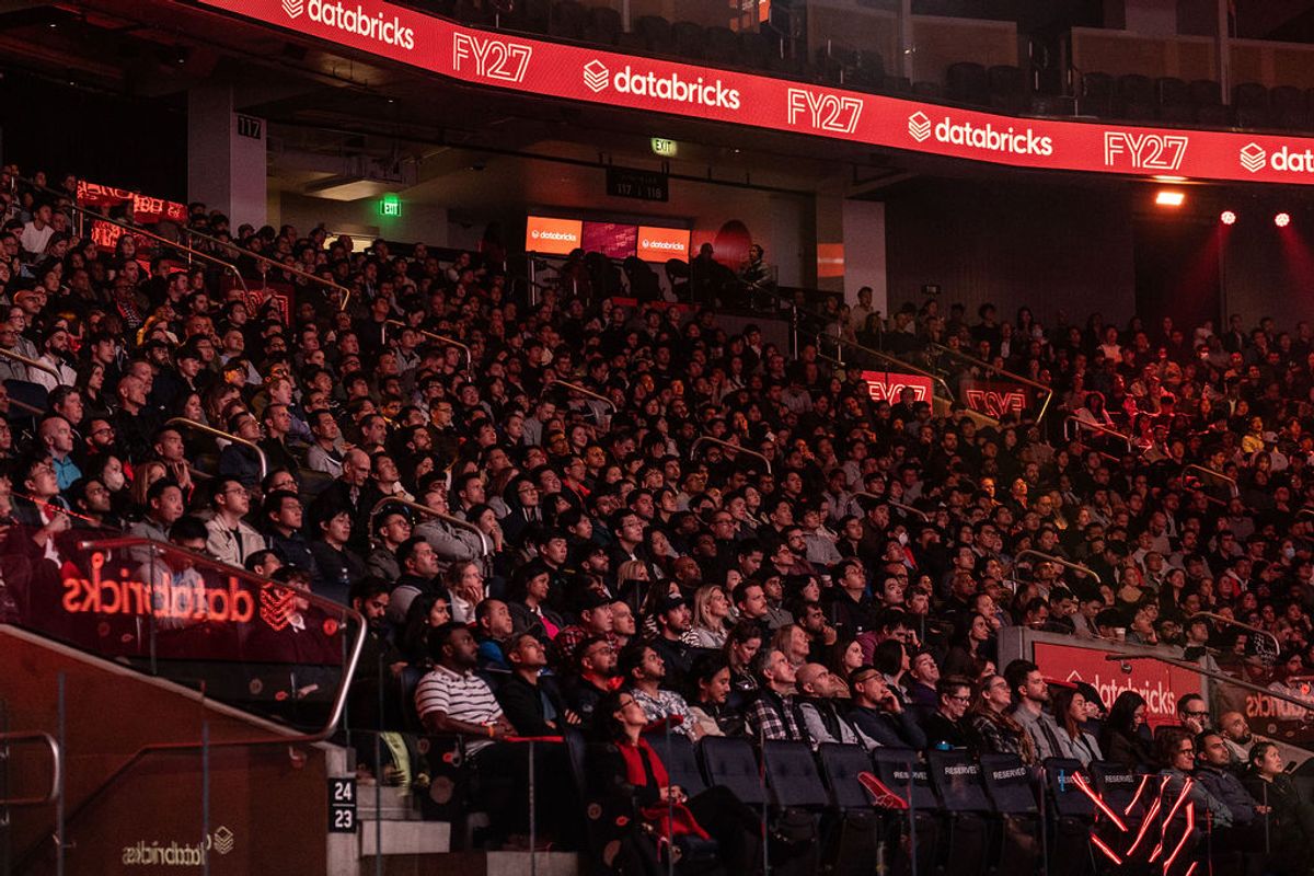Large crowd of attendees seated in tiered seating at Databricks FY27 conference venue with red lighting
