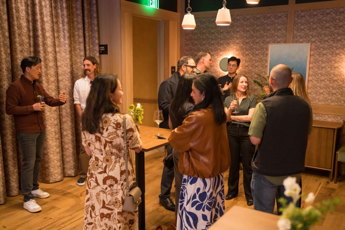People networking and socializing in a modern interior space with pendant lighting and patterned wallpaper.