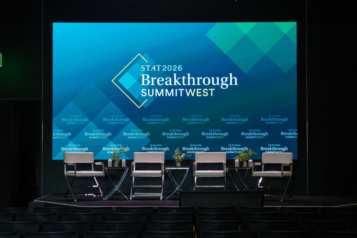 Stage with six empty chairs and table setup beneath large screen displaying STAT2026 Breakthrough Summit West.
