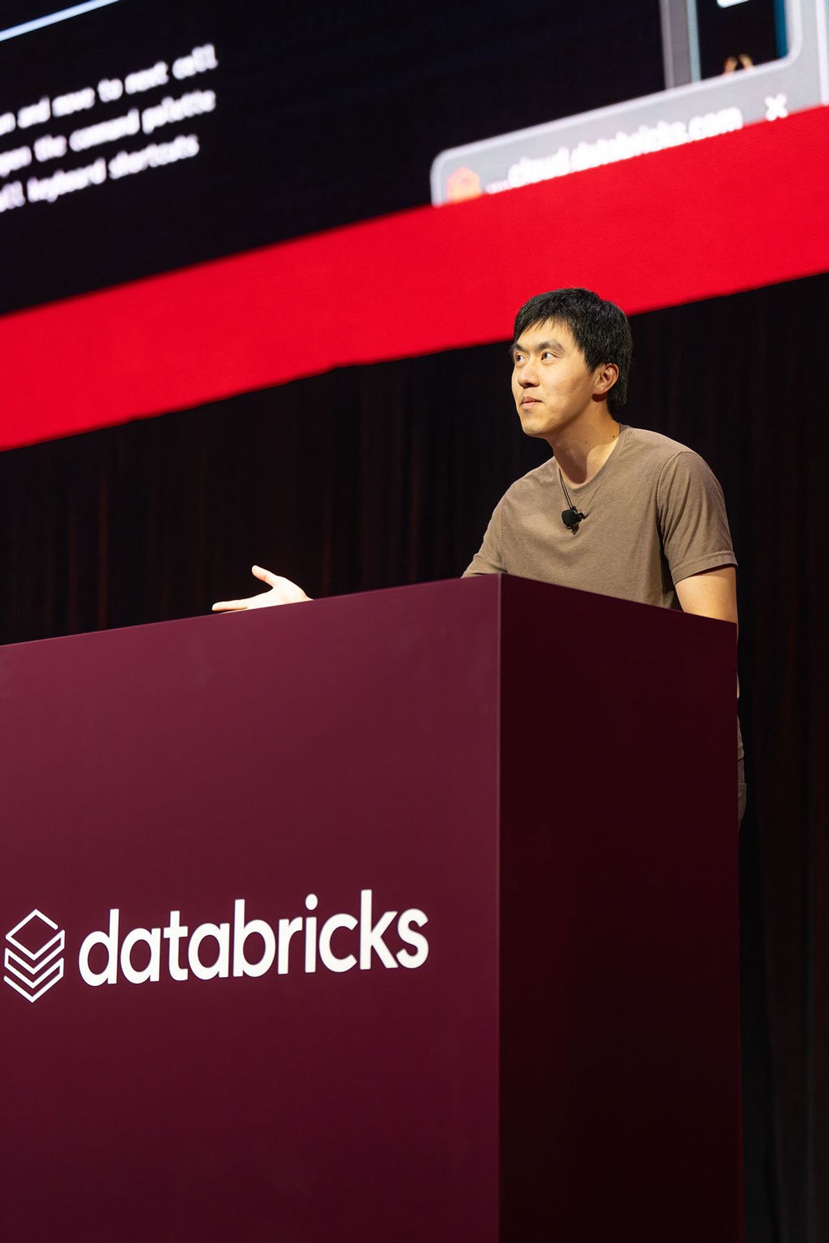 Speaker presenting at Databricks conference podium with red and black backdrop