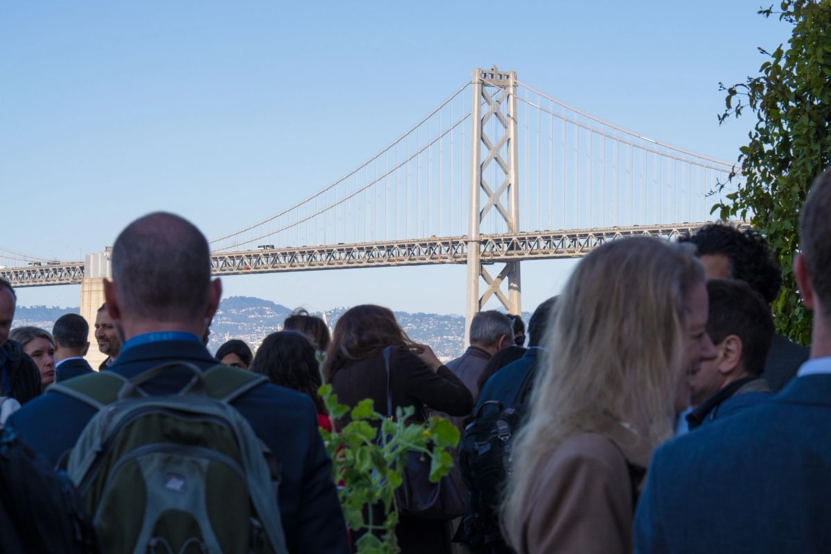 Conference attendees gather outdoors with suspension bridge visible in background