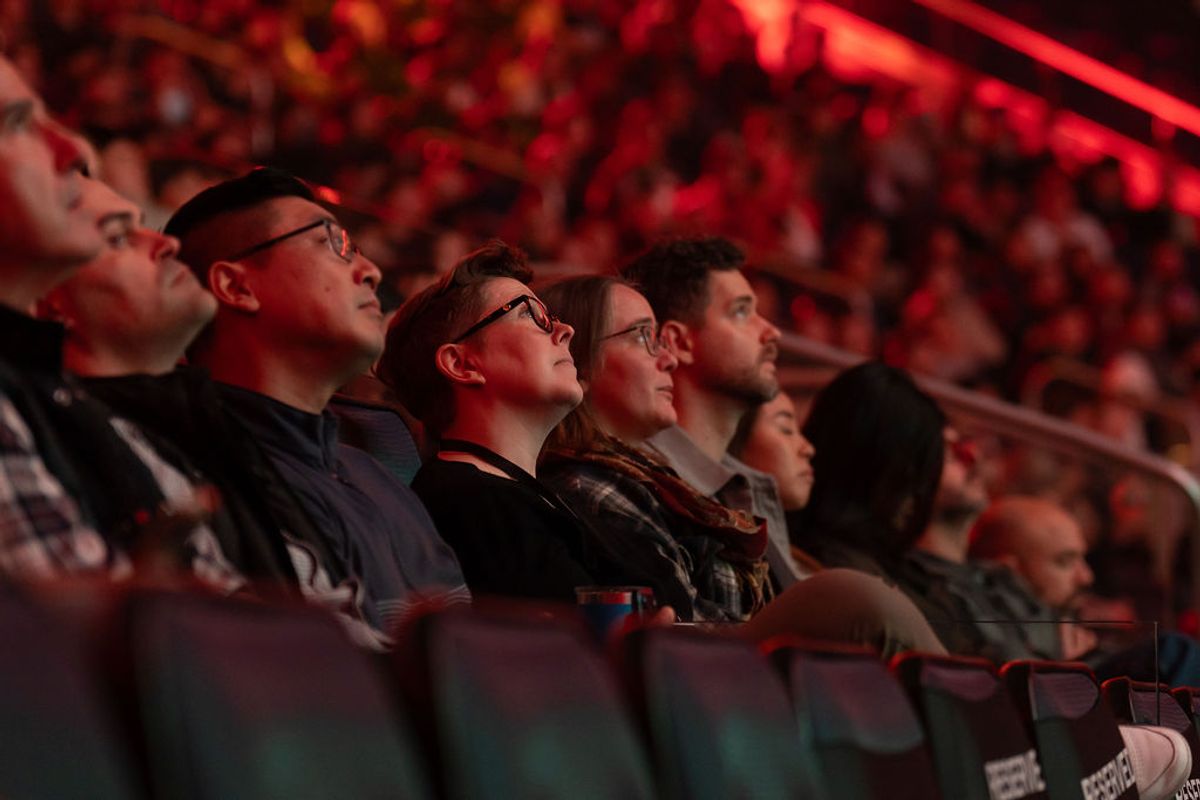 Audience members sitting in red-lit auditorium seats looking up attentively during a conference presentation