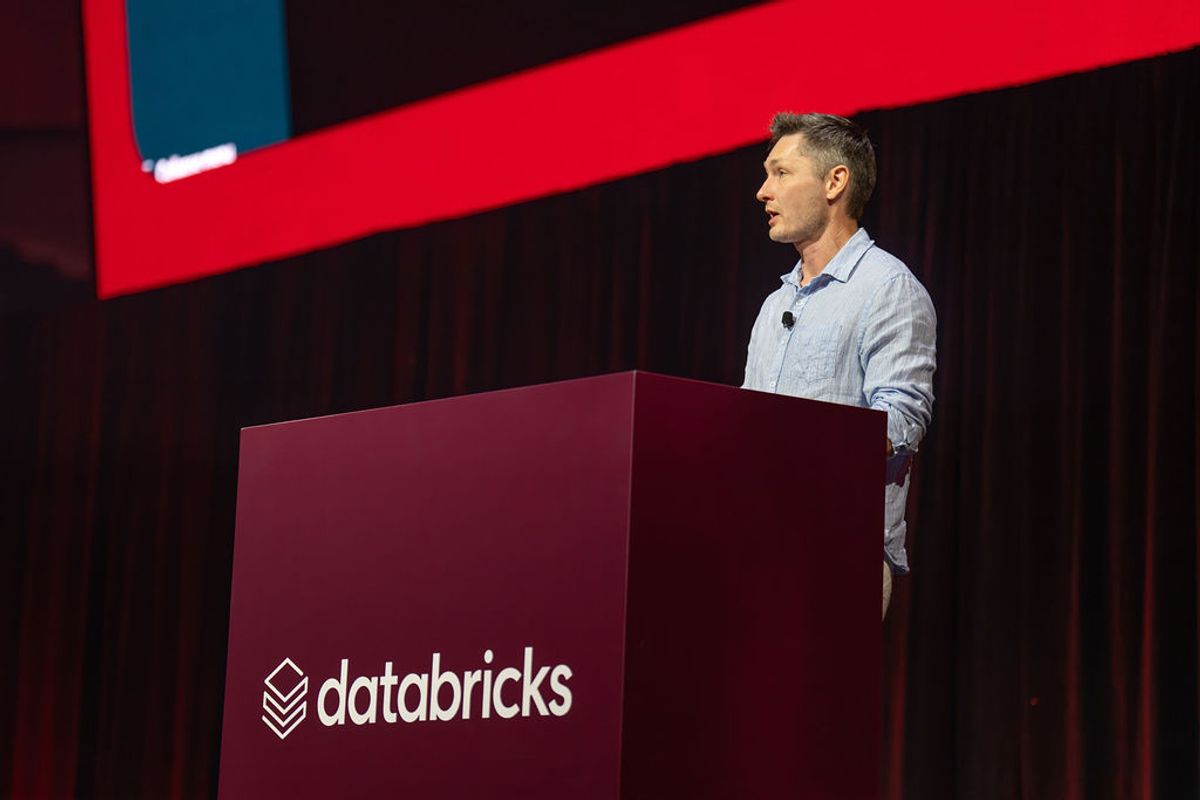 Speaker presenting at Databricks conference podium with red stage lighting and branded backdrop