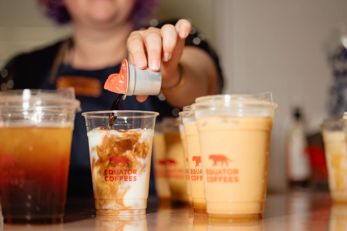 Barista pouring syrup into iced coffee drinks at Equator Coffees, multiple beverages visible on counter